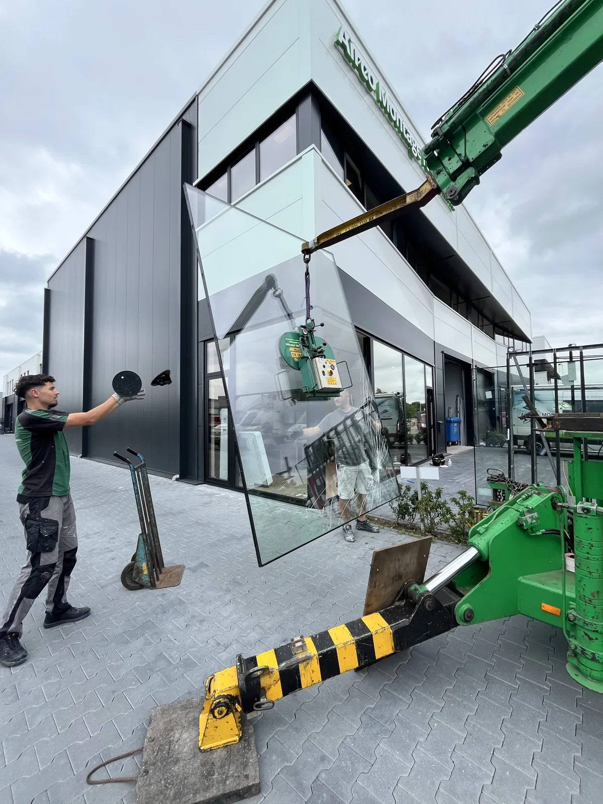 Glasbedrijf Groningen hijst een grote glasplaat met een kraan bij een bedrijfspand