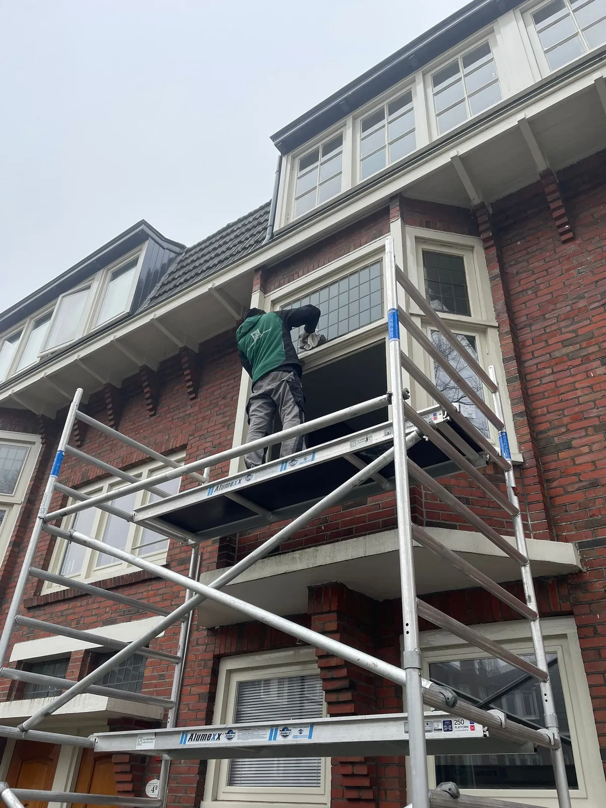 Glaszetter van Glasbedrijf Groningen plaatst glas vanaf een rolsteiger bij een jaren-30 woning